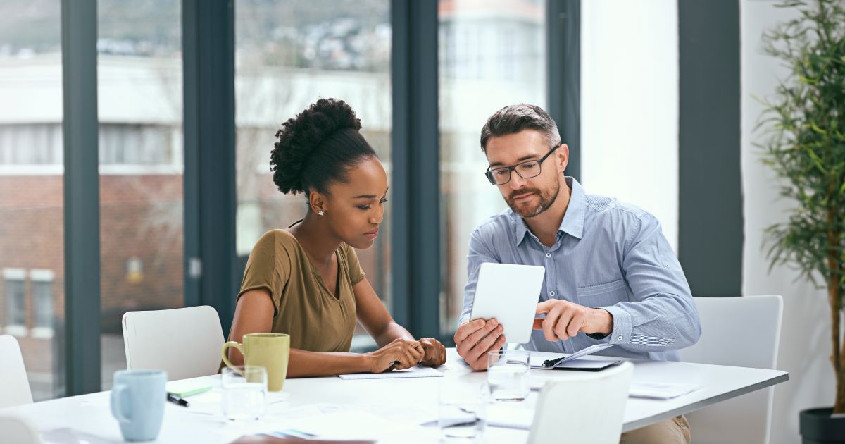 An early career employee and a manager reviewing a report while seated at a conference room table.