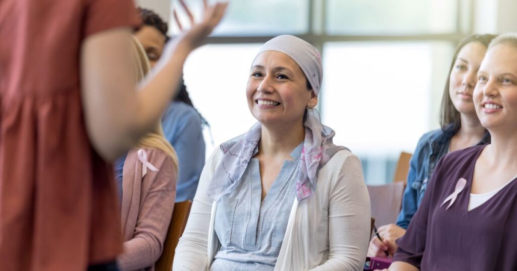 Woman wearing a headscarf, who is a cancer patient, smiles and sits in a group listening to a presenter