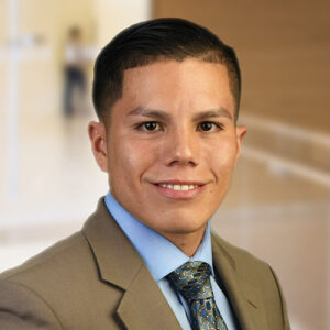 BMS employee and veteran, Ricardo Sanchez, wears a beige suit jacket with a light blue shirt and tie