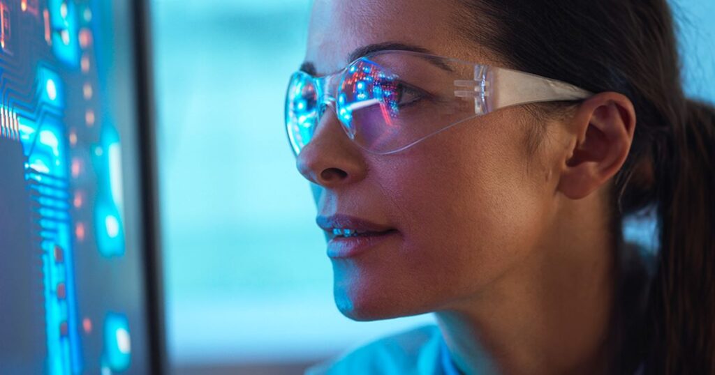 Female scientist in goggles looking at high tech computer screen