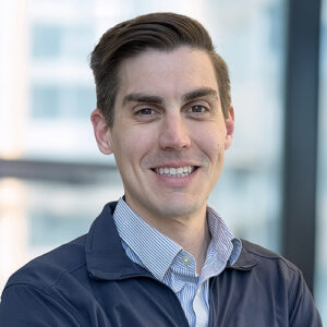 Thomas Struble, BMS employee stands smiling in an office setting in a shirt and dark zip jacket